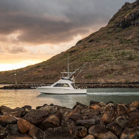 Boat on water near rocky shore and hillside at sunset with cloudy sky.