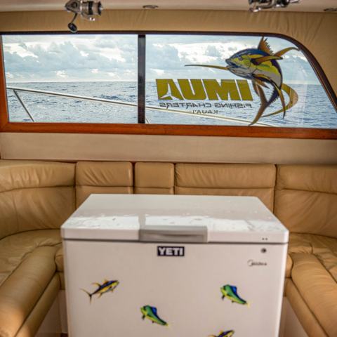Boat interior with beige seating, white Yeti cooler, and ocean view through windows.