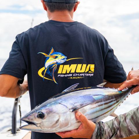 Man in a fishing charter shirt holding a large fish on a boat.