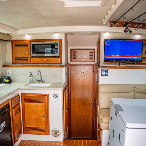 Interior of a boat cabin with wooden cabinets, a counter, microwave, TV, sofa, and cooler.