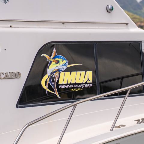 Boat with 'IMUA Fishing Charters' logo and marlin graphic on window.